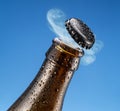 Opening beer bottle on blue background. Gas cloud going out of the beer bottle blowing the cap Royalty Free Stock Photo