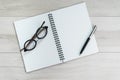 Opening white blank paper note book with pen on the right and glasses on the left on light grey wooden table background with copy Royalty Free Stock Photo