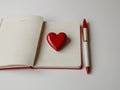 Openning note book white blank page with pen and lovely red ceramic heart shape on white background