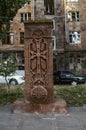 Ancient openwork khachkar made of red tuff with a figured arch over the cross and openwork ornament in a circle on the Alley of st