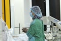 At the operating room. Female surgeon in the mask over face standing near patient plate and disinfecting hands