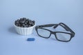 Ophthalmic concept close up. Glasses, blueberries and blueberry vitamin on a blue background. Natural products to improve and Royalty Free Stock Photo