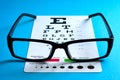 Ophthalmological exam, healthy eyes and ophthalmology concept with a pair of vision glasses and an eye chart isolated on blue Royalty Free Stock Photo