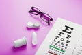 Ophthalmologist accessories glasses, lenses and vitamins with a test target for vision correction on a pink background Royalty Free Stock Photo