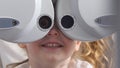 Ophthalmology clinic - smiling little blonde girl checks vision eyesight, close up
