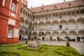 Opocno castle, renaissance chateau, courtyard with arcades and red facade, green lawn with statue and flowers in foreground, sunny