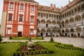 Opocno castle, renaissance chateau, courtyard with arcades and red facade, green lawn with statue and flowers in foreground, sunny