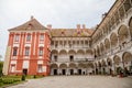 Opocno castle, renaissance chateau, courtyard with arcades and red facade, green lawn with statue and flowers in foreground, sunny