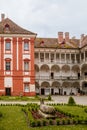 Opocno castle, renaissance chateau, courtyard with arcades and red facade, green lawn with statue and flowers in foreground, sunny