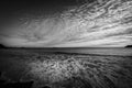 Opposing patterns of clouds in sky and backwash of waves on sand