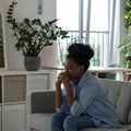 Oppressed African American woman with sad face sits on sofa thinking about future. Life trouble.