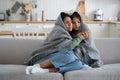 Oppressed unhappy woman and teen girl are trying to keep warm wrapped in warm blanket sits on couch