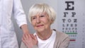 Optician comforting elderly woman during eyesight examination, health care