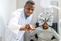 Optician doing optometry eye exam for black african american teen girl patient. Male optometrist with phoropter while examining Royalty Free Stock Photo
