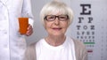 Optician giving fresh carrot juice to happy aged lady, maintaining good vision Royalty Free Stock Photo