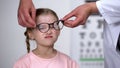 Optician putting corrective glasses on upset girl, childhood eye diseases