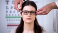 Optician putting on female patient new eyeglasses, appropriate lenses, store