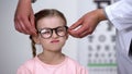 Optician putting glasses on little girl to make vision better, professional help