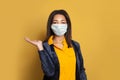 Optimistic African American woman in face mask on yellow background. Black girl in medical mask showing empty open hand