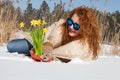 Optimistic curly haired woman admiring bouquet of yellow narcissus while lying in snow