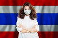 Optimistic doctor in protective mask against national flag Thai. Flu epidemic and virus protection concept