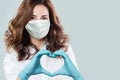 Optimistic doctor woman in protective mask making heart. Healthcare, medicine and treatment concept