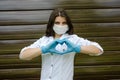 Optimistic doctor woman in protective mask making heart. Healthcare, medicine and treatment concept