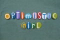 Optimistic girl, creative message composed with multi colored stone letters over green sand