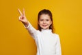 Optimistic girl kid showing peace gesture against bright yellow background Royalty Free Stock Photo