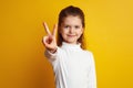 Optimistic girl kid showing peace gesture against bright yellow background Royalty Free Stock Photo