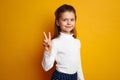 Optimistic girl kid showing peace gesture against bright yellow background Royalty Free Stock Photo