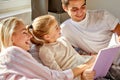 Positive caucasian parents read book with child on bed