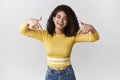 Optimistic smiling happy good-looking woman curly-haired wearing stylish cropped yellow top pointing down nodding