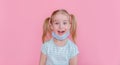 Optimistic, smiling happy little girl taking off the medical mask from face on a pink background with hand up showing end of the