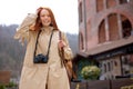 Optimistic woman with long red straight hair wearing beige coat walking in town Royalty Free Stock Photo