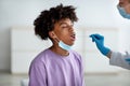 Oral coronavirus PCR test. Doctor using sterile swab to take covid virus sample from black teenager at clinic Royalty Free Stock Photo