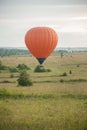 An orange air balloon flying over the field using heat technology