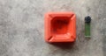 Orange ashtray with cigarette residue and green lighter on a concrete surface. Royalty Free Stock Photo
