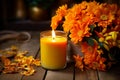 Orange autumnal flowers in vase and lit candle on wooden background