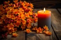 Orange autumnal flowers in vase and lit candle on wooden background