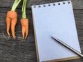 Orange Baby carrot look like woman shape on wooden background and space notebook and pen
