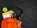 Orange backpack with school supplies on a black concrete background. The concept of the school