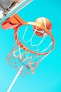 An orange basketball ball in hoop on a blue sky background. A ball flying into the basket. Royalty Free Stock Photo