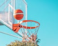 An orange basketball ball in hoop on a blue sky background. A ball flying over the basket Royalty Free Stock Photo