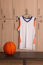 Orange basketball ball on wooden bench and hanger with uniform in locker room