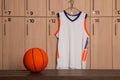 Orange basketball ball on wooden bench and hanger with uniform in locker room