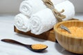 Orange bath salt in a wooden bowl and spoon and three white towels on a wooden box on a white marble table Royalty Free Stock Photo