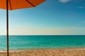 Orange beach umbrella on golden sand beach by the sea with emerald green sea water and blue sky and white clouds. Summer vacation Royalty Free Stock Photo