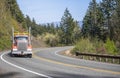 Orange big rig semi truck with oversized load sign on the roof running uphill on the winding road