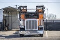 Orange and black car hauler big rig semi truck with empty semi trailer standing on the warehouse parking lot